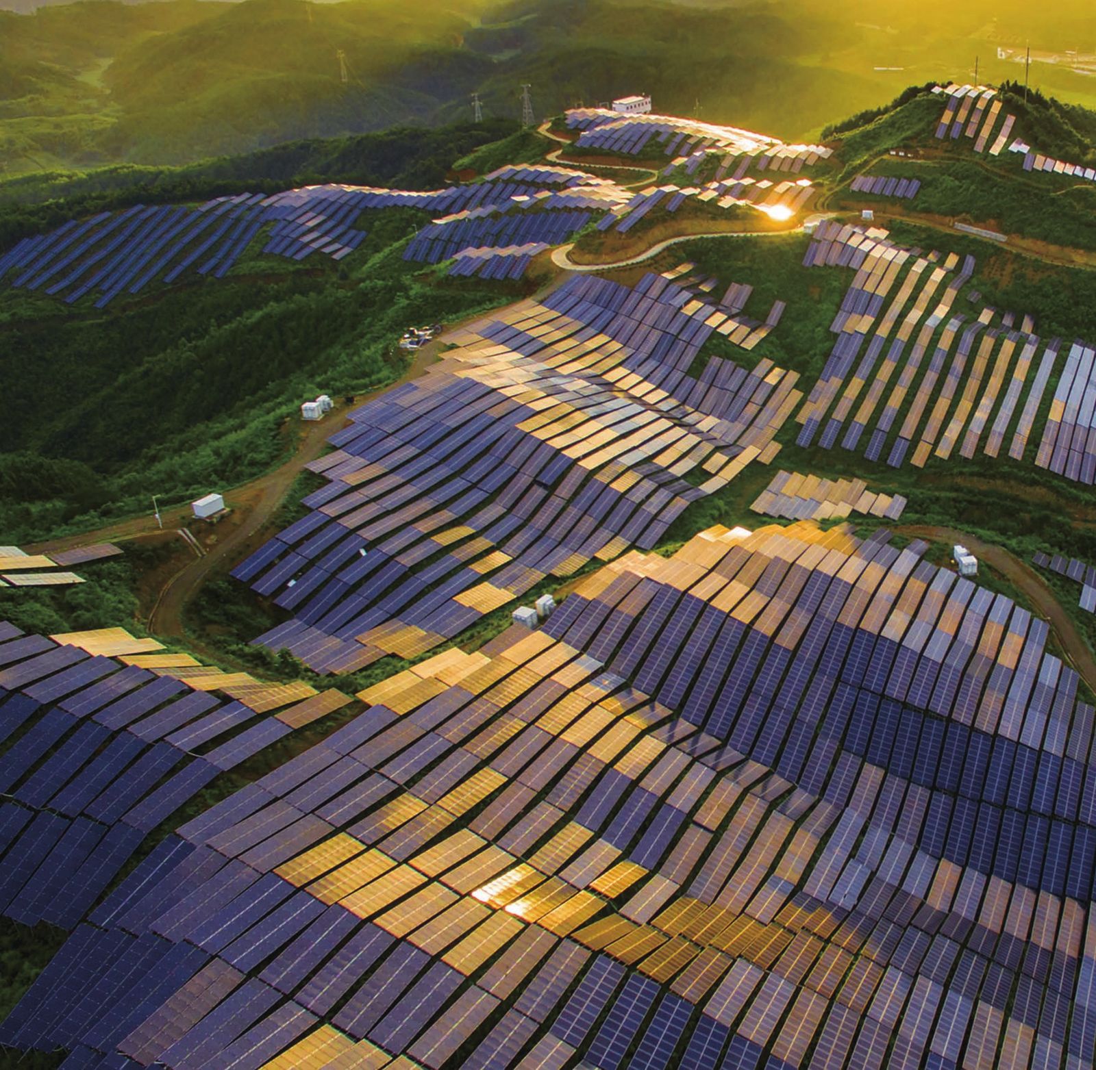 Aerial view of a large solar power plant on green hills at sunset