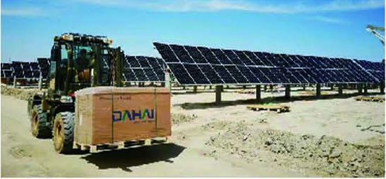A loader carrying a pallet of DAHAI modules past a ground-mounted solar plant